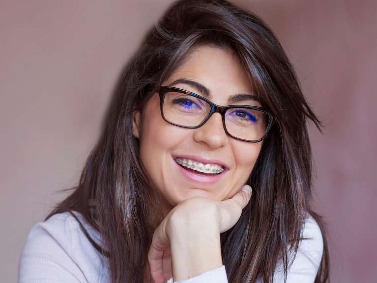 Smiling woman with glasses highlights the link between orthodontics and overall health.